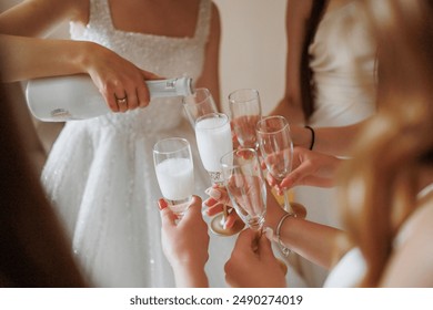 A group of women are celebrating a special occasion by toasting with champagne. One woman is pouring the champagne into the glasses while the others hold their glasses up to their lips - Powered by Shutterstock