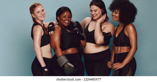 Group of women of different race and body size in sportswear standing together. Diverse women with sports equipment looking at camera against grey background.