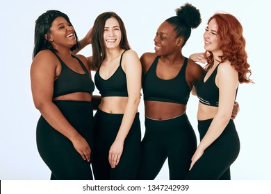 Group of women of different race, figure and size in sportswear standing together, chatting and laughing against white background.