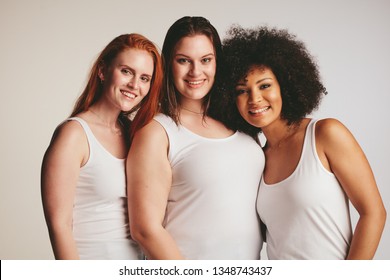 Group of women of different size dressed in white tank top standing together. Three diverse women looking at camera against white background.