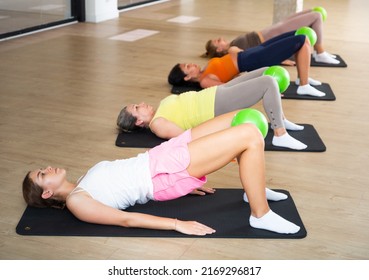 Group of women doing hip bridge exercise with small pilates ball