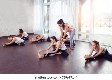 Group women doing stretching and yoga exercises with instructor in fitness class against window