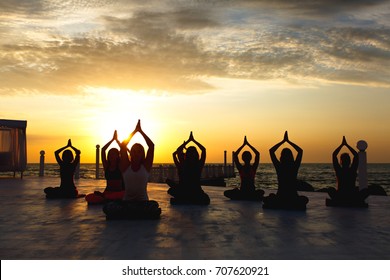 The group of women doing yoga at sunrise near the sea