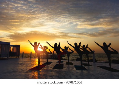 The group of women doing yoga at sunrise near the sea - Powered by Shutterstock