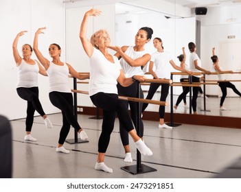 Group of women engaged in ballet in a dance studio perfoms an exercise near the ballet barre, where the choreographer helps ..to coordinate the movements correctly - Powered by Shutterstock