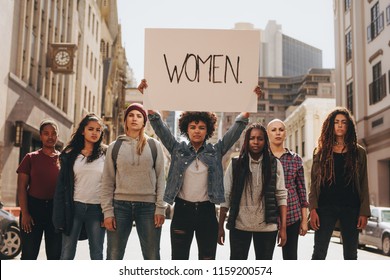 Group Of Women Marching On The Road In Protest. Young Woman Holding A Protest Sign About Women Empowerment