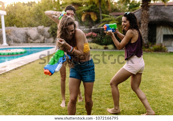Group of women at the poolside\
having  water gun battle. Female friends playing with water\
guns.