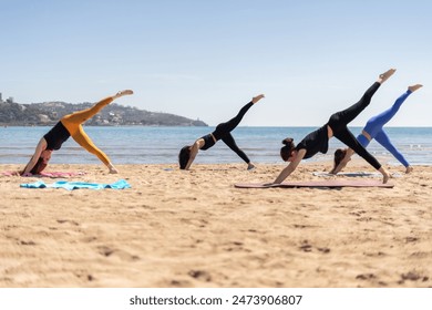Group of women practicing pilates on the beach, performing leg lift exercises on mats with the ocean and distant hills in the background under a clear blue sky. - Powered by Shutterstock