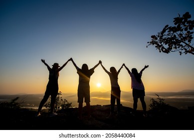Group of women rise their hands up and hold together looking to the sunrise over Pha Chanadai cliff and mountain ,Pha Taem National park, Ubonratchathani, Thailand