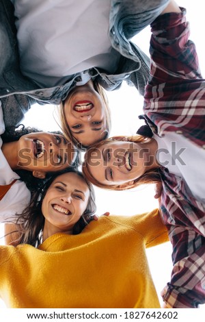 Group of women standing in a huddle with their heads touching. Low angle view of cheerful females forming a huddle and looking at camera.