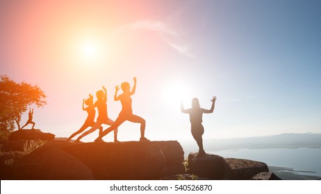 The Group Women With Yoga Posture On The Mountain At Sunset; Silhouette Of Gorgeous Young Woman Practicing Yoga Outdoor.