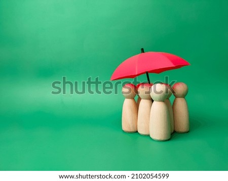 A group of wooden dolls are hiding under a red umbrella, protecting wooden peg dolls, planning, saving families, preventing risks and crises, health care and insurance concepts.