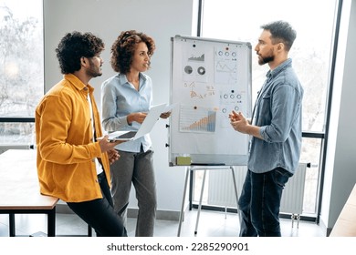 Group work concept. Successful creative colleagues are working together on a new project, standing near white marker board with graphs in the office, predicting income, analyzing risks, setting goals - Powered by Shutterstock