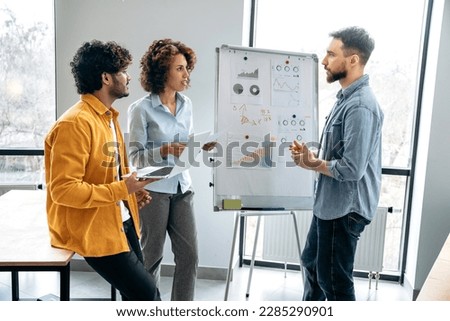 Group work concept. Successful creative colleagues are working together on a new project, standing near white marker board with graphs in the office, predicting income, analyzing risks, setting goals