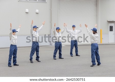 A group of workers doing exercises in front of a factory
