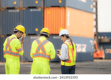 Group of workers in the import and export industry use walkie talkies to communicate with drivers of reach stacker containers in an empty container warehouse.
