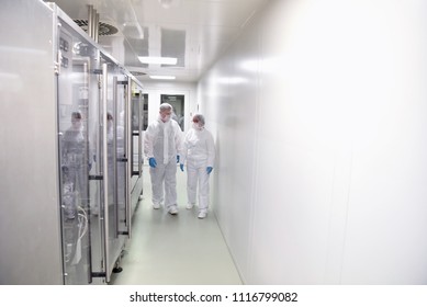 Group Of Workers In Protective Clothing In A Sterile Room Of A Factory To Honor And Develop Drugs 