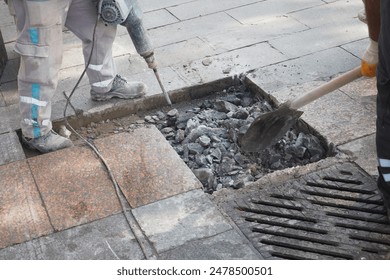 A group of workers using a jackhammer to break and remove concrete sections on a construction site
