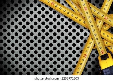 Group of yellow and orange tape measures on a silver metal background with many holes and copy space, photography. - Shutterstock ID 2256971603