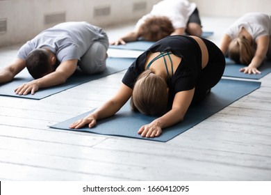 Group Yoga Session In Sport Club Studio Concept. People In Comfy Activewear Lying Resting Performing Balasana Relaxation Exercise, Child Pose Helps Reduce Fatigue And Stretching Lower Back, No Stress