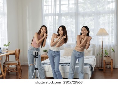 Group of young adult Asian females with beautiful, healthy skin, are having fun at home. They are dancing and recording videos on their smartphones to create content to upload on social media - Powered by Shutterstock