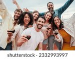 Group of young adult best friends having fun toasting a red wine glasses at rooftop reunion or birthday party, drinking alcohol. Happy people enjoying on a social gathering celebrating together. High