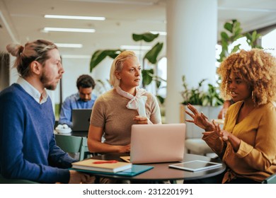 A group of young adult coworkers are in a cafeteria working on a project during their break. - Powered by Shutterstock