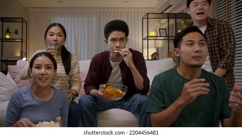 Group of young adult friend man and woman asia people sit at sofa couch joy night party fun game FIFA world cup live TV at home eat snack bowl drink beer bottle glass jump mad happy win exult face - Powered by Shutterstock