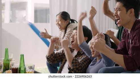 Group of young adult friend man and woman asia people sit at sofa couch joy chanting party fun game FIFA world cup live TV at home eat snack bowl drink beer bottle glass jump mad happy win exult face. - Powered by Shutterstock