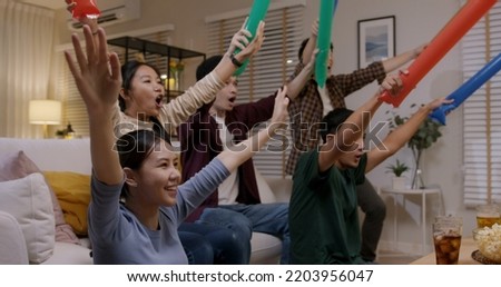 Group of young adult friend man and woman asia people sit at sofa couch joy party fun game FIFA world cup live TV at home chanting hand raised sign jump mad happy win exult face.