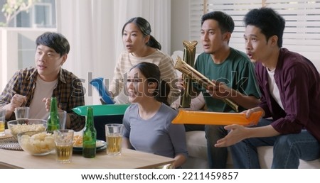 Group of young adult friend man and woman asia people sit at sofa couch joy chanting party fun game FIFA world cup live TV at home eat snack bowl drink beer bottle glass jump mad happy win exult face.