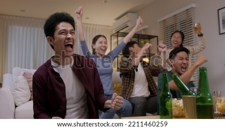 Group of young adult friend man and woman asia people sit at sofa couch joy night party fun game FIFA world cup live TV at home eat snack bowl drink beer bottle glass jump mad happy win exult face