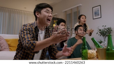 Group of young adult friend man and woman asia people sit at sofa couch joy night party fun game FIFA world cup live TV at home eat snack bowl drink beer bottle glass jump mad happy win exult face