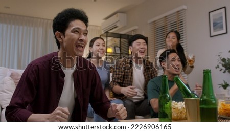 Group of young adult friend man and woman asia people sit at sofa couch joy night party fun game FIFA world cup live TV at home eat snack bowl drink beer bottle glass jump mad happy win exult face.