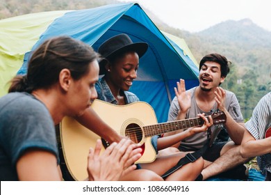 Group Of Young Adult Friends In Camp Site Playing Guitar And Ukelele And Singing Together 