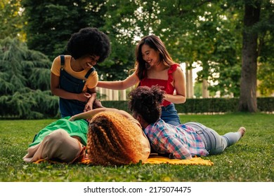 A group of young adult girls are playful and tickling each other rolling on the park lawn