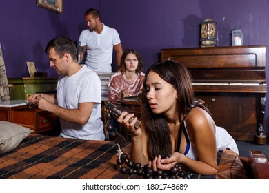 Group Of Young Adults Inspecting Wooden Rosary, Trying To Find Solution Of Conundrum In Escape Room With Antique Furnitures..