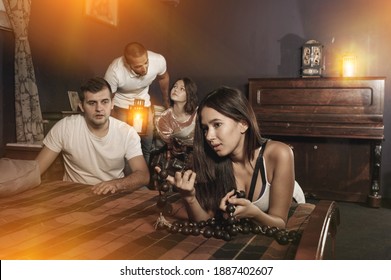 Group Of Young Adults Inspecting Wooden Rosary, Trying To Find Solution Of Conundrum In Escape Room With Antique Furnitures