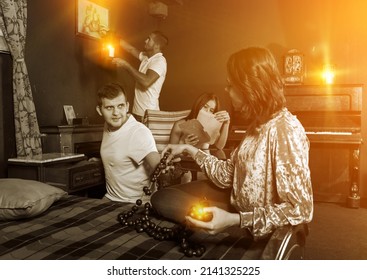 Group Of Young Adults Inspecting Wooden Rosary, Trying To Find Solution Of Conundrum In Escape Room With Antique Furnitures..