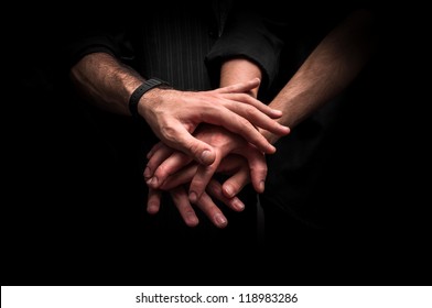 Group of young adults making a pile of hands against dark background