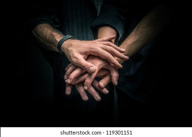 Group of young adults making a pile of hands against dark background