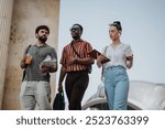 Group of young adults strolling outdoors, holding beverages and notebooks, engaged in conversation and study.