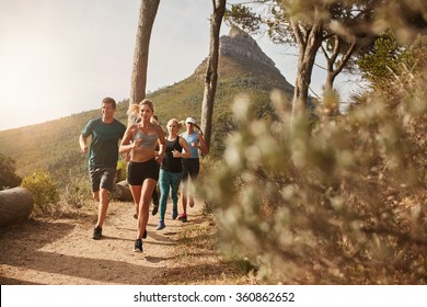 Group of young adults training and running together through trails on the hillside outdoors in nature. Fit young people trail running on a mountain path. - Powered by Shutterstock