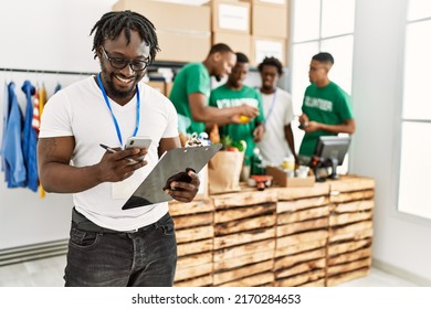 Group of young african american volunteers working at charity center. Man smiling happy using smartphone.