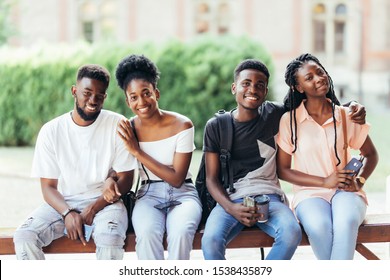 group of young african friends hanging out together outdoors on a bench and laughing as they discuss