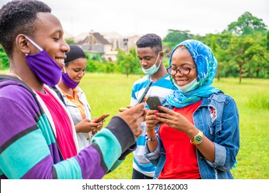 a group of young african people using their mobile phones simultaneously, smiling, wearing face masks, with physical distancing