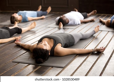 Group of young afro american and caucasian sporty people practicing yoga lesson lying in Dead Body pose, Savasana exercise, working out, resting after practice, indoor close up, studio - Powered by Shutterstock