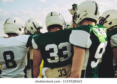 Group Of Young American Football Players Standing Together With Their Arms Raised In A Huddle Before A Game