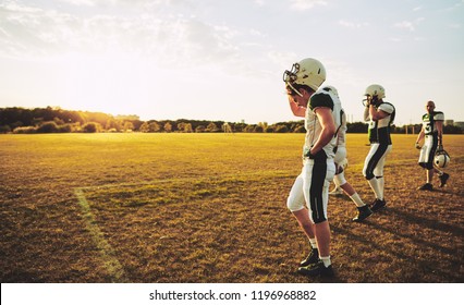 Group of young American football players taking off their helmets and walking off the field after a late afternoon practice - Powered by Shutterstock