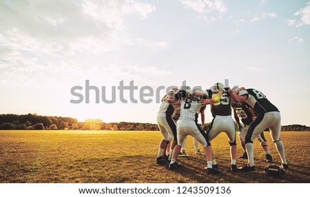 Group of young American football players standing in a huddle together on a sports field in the afternoon discussing before a game